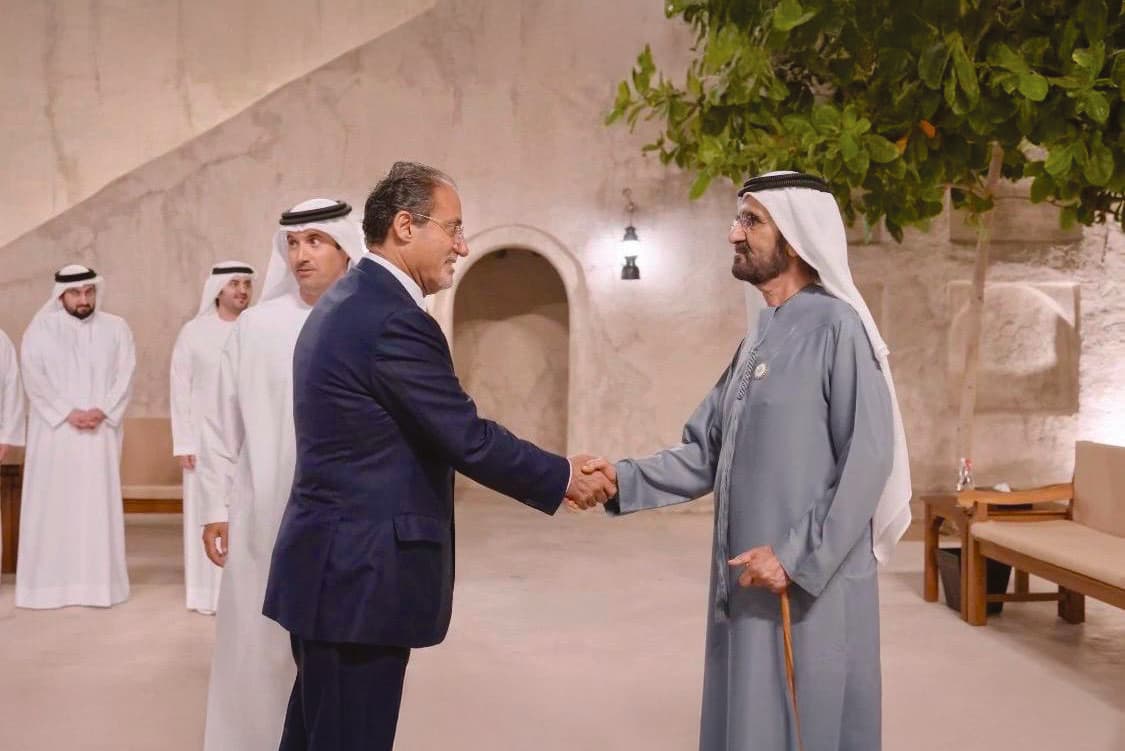 Moafaq A. Al Gaddah standing beside an official in front of flags at a diplomatic meeting.